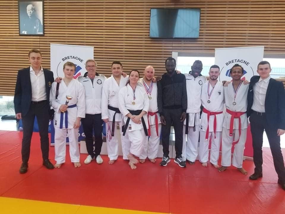 Photo d’équipe après une compétition : karatékas médaillés et encadrants alignés sur le tatami