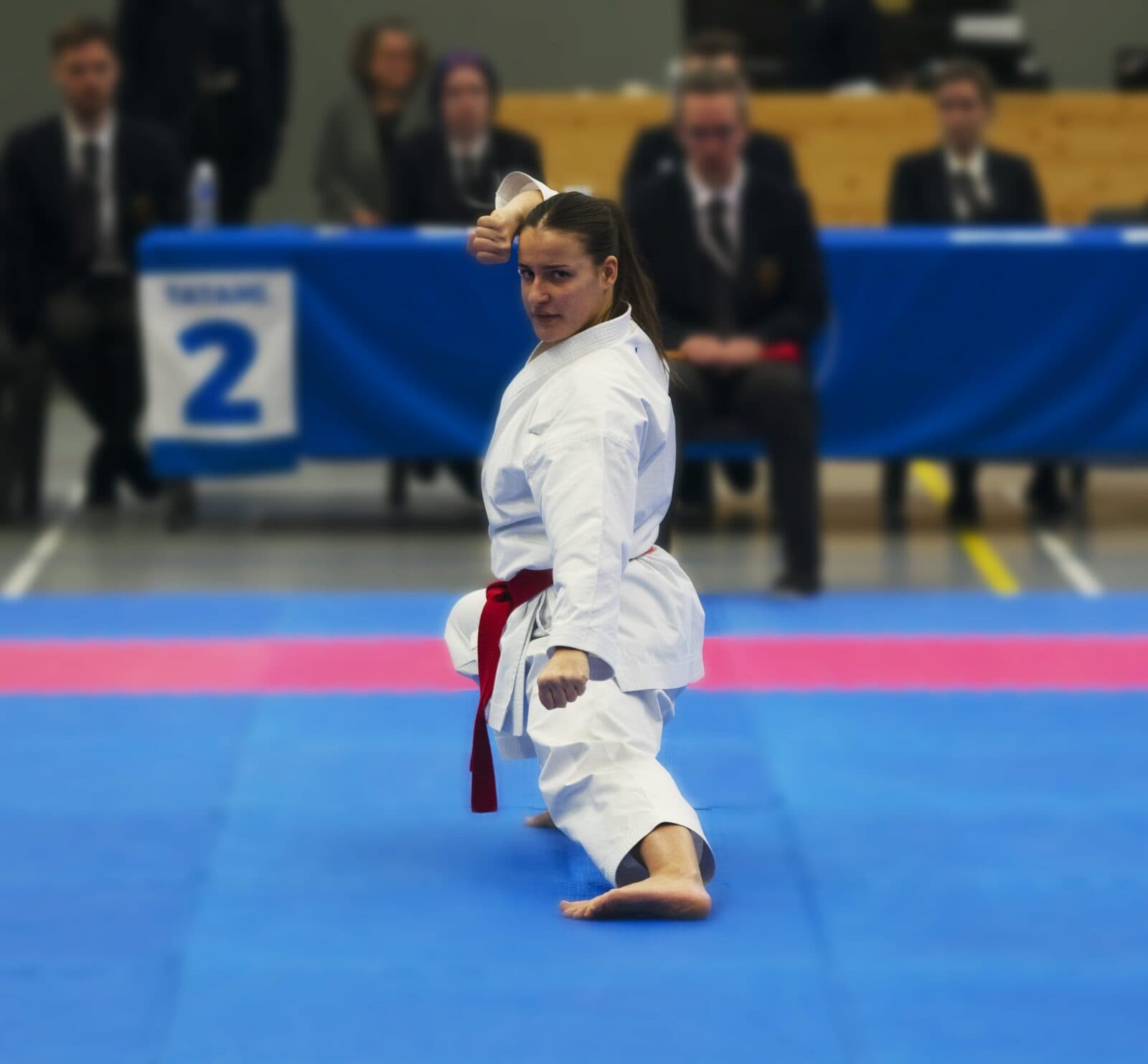 Karatéka ceinture rouge exécutant un kata sur le tatami devant le jury