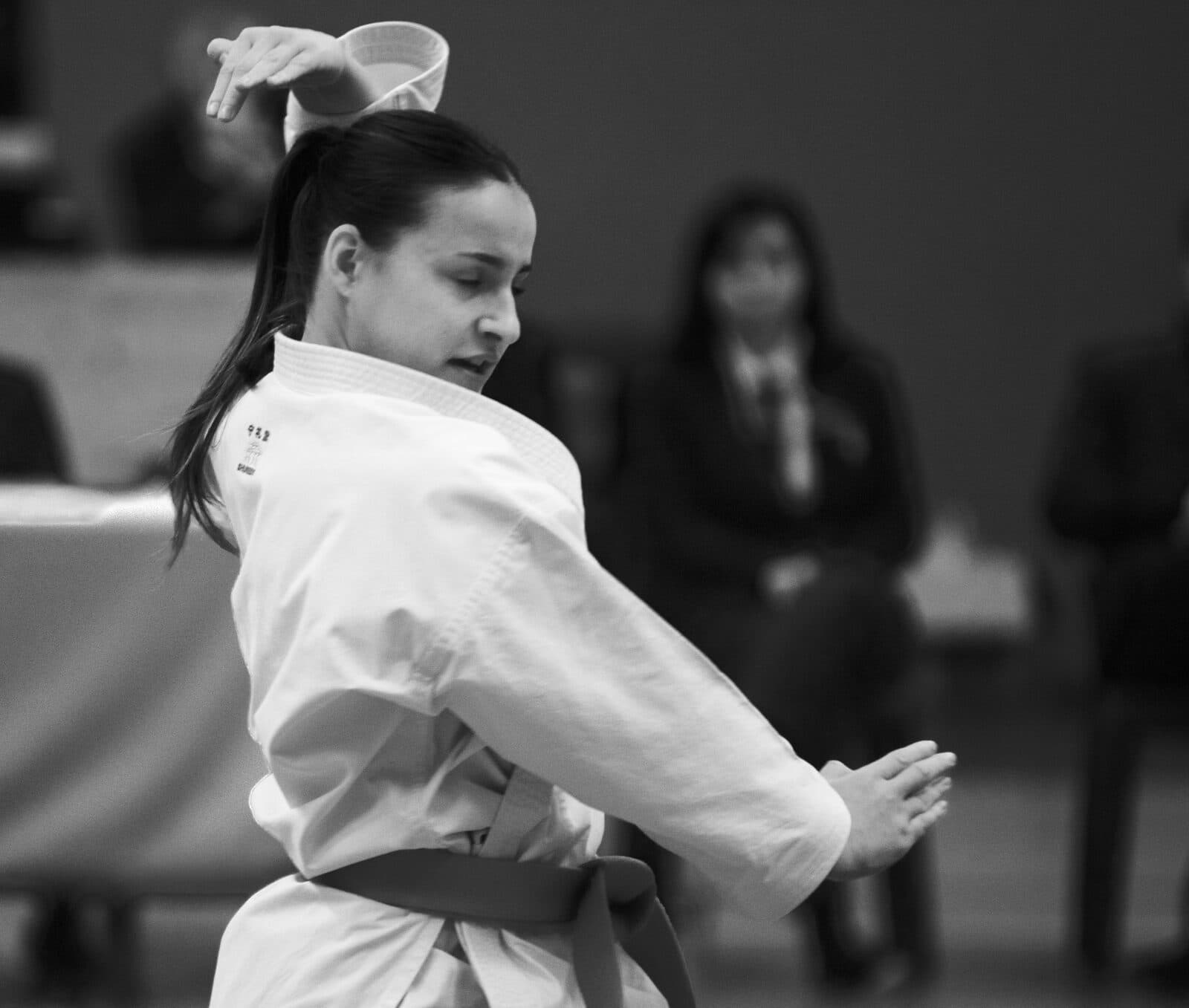 Karatéka exécutant un kata en compétition, photographiée en noir et blanc dans un mouvement de rotation