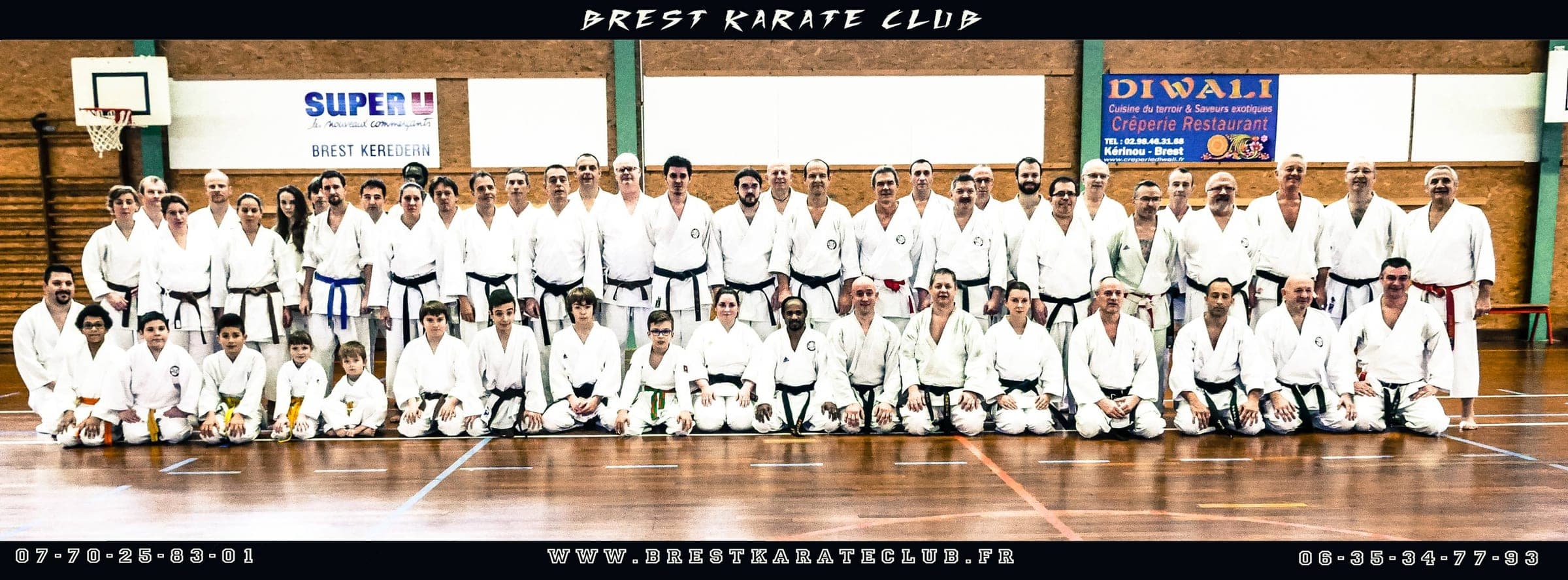 Photographie de groupe du Brest Karaté Club en gymnase : une soixantaine de pratiquants de tous âges en karategi, debout et agenouillés sur trois rangs, sous un bandeau « BREST KARATE CLUB » ; le bas de l’image rappelle les téléphones du club et l’adresse de son site